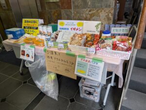テーブルの上には、長期保存食 IZAMESHI（イザメシ）シリーズや、そのまま食べられるパスタ、そして災害時用トイレキット「ベストトイレ」などが並んでいます。価格は多くが648円〜756円ほど。