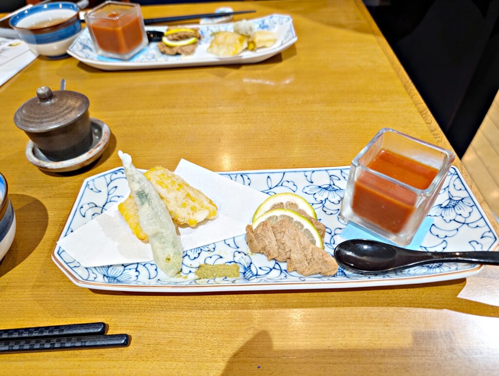 「和食ランチの前菜盛り合わせ。天ぷら、レモンを添えた肉料理、トマトソースが並ぶ上品な器」